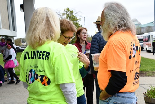 a group of 4 volunteers stand outside chatting 3 are in their brightly colored lime green volunteer branded t-shirts one is wearing a bright orange volunteer shirt and he has very long hair and a beard, everyone looks very happy