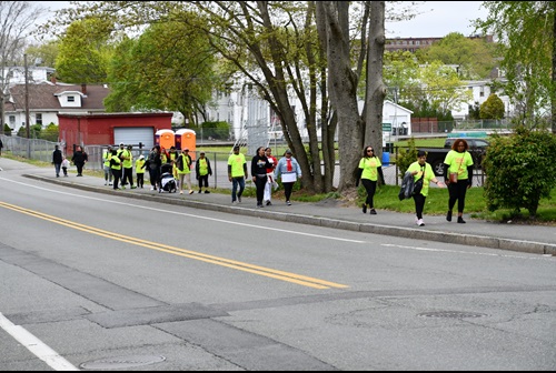 a group of about 20 walk participants of various ages, predominantly people of color are making their way at varying paces down a sidewalk, almost all are wearing matching lime green matching team t-shirts